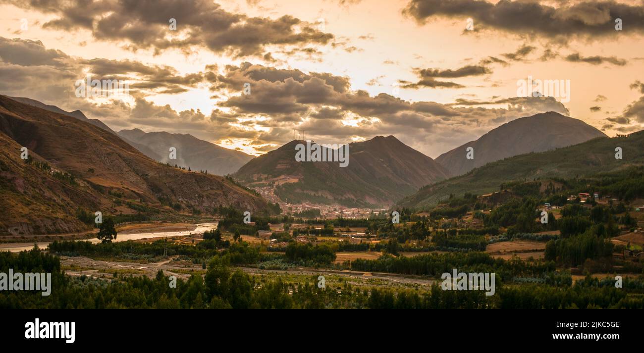 nearby forest with river and distant mountains, sunset in cloudy sky, urcospampa, cusco, peru Stock Photo