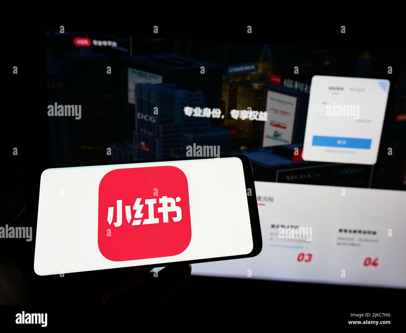 Person holding smartphone with logo of Chinese social media company Xiaohongshu on screen in front of website. Focus on phone display. Stock Photo