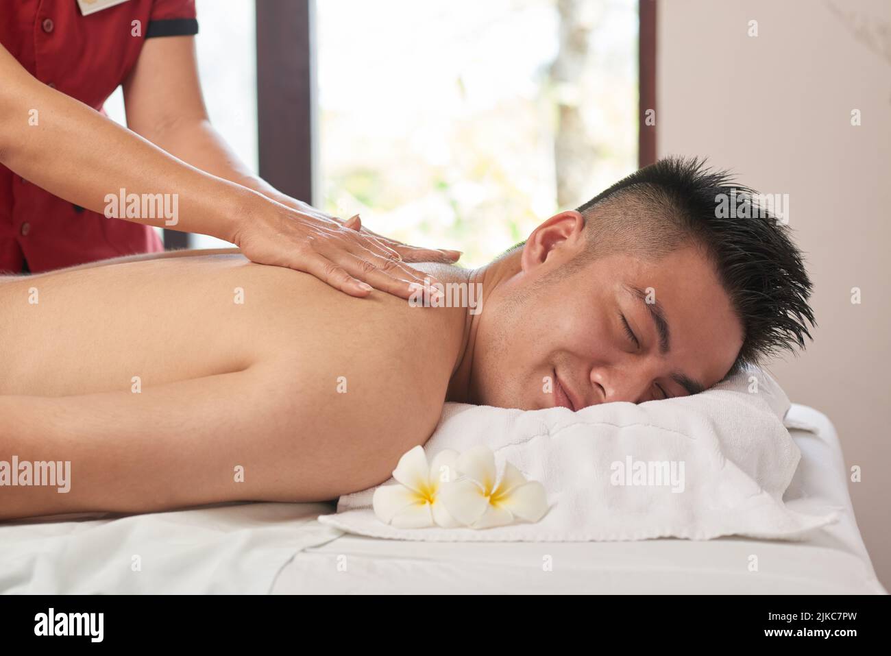 Handsome Asian man with closed eyes getting back massage while lying on tre...