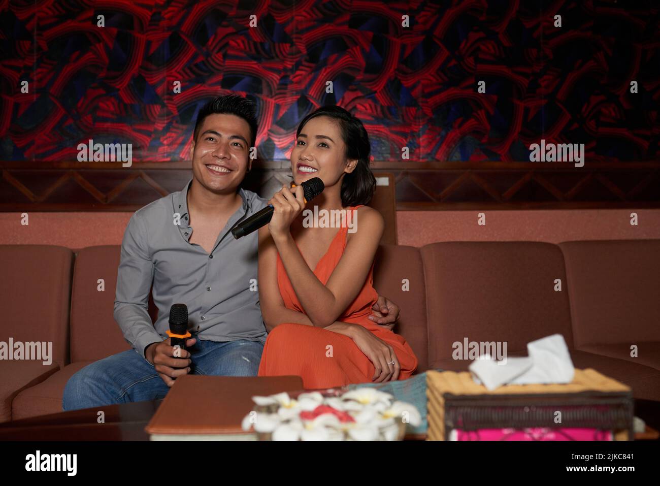 Joyful young couple having fun in karaoke night club they sitting on