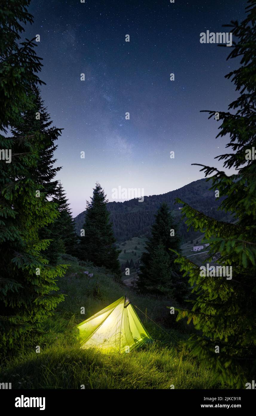 A vertical shot of an illuminated green tent in the Italian Alps under ...