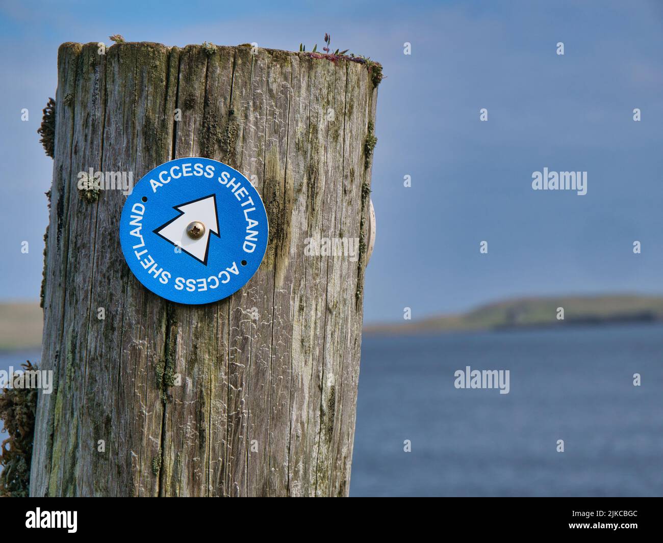 Fixed to a wooden post on the coast, a blue and white Access Shetland sign near Sandwick in Shetland, UK shows the way to walkers and hikers. Stock Photo
