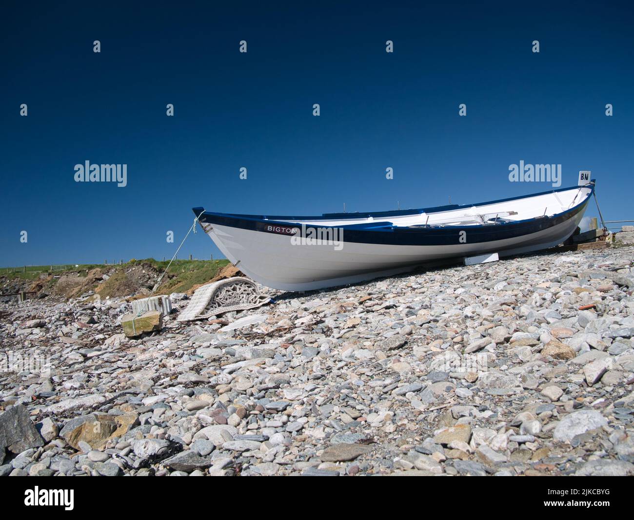 A traditional wooden, clinker built blue and white fishing boat on a pebble beach in southern Shetland, UK. Taken on a sunny day with a cloudless sky. Stock Photo
