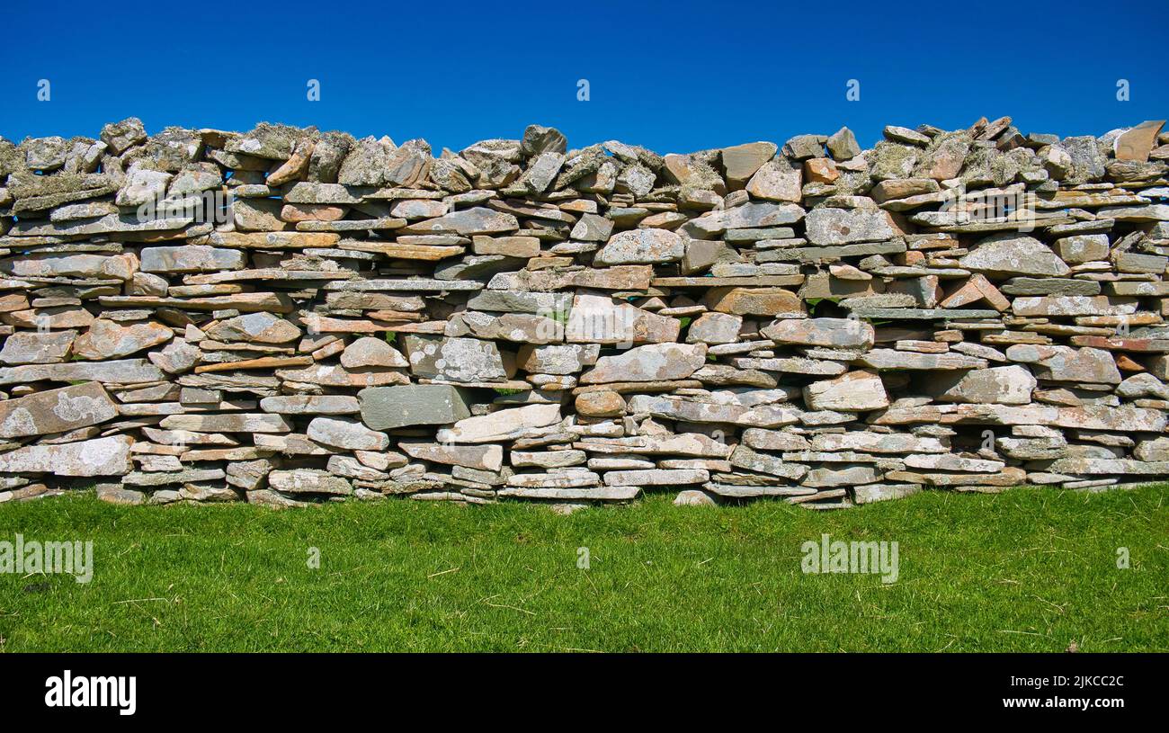 A colourful dry stone wall on a sunny day between a clear blue sky and green grass. Stock Photo