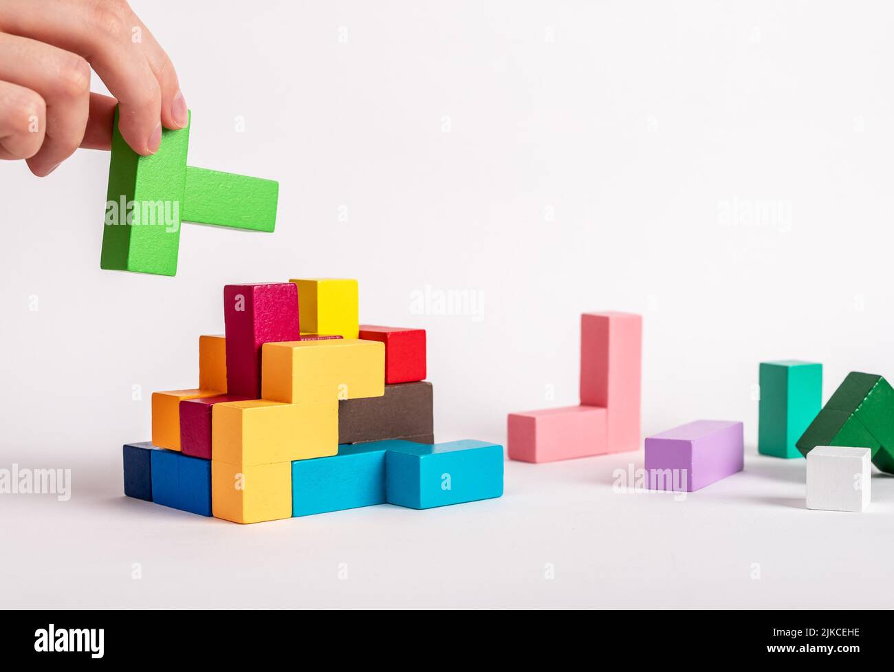 Hand assembling tetris puzzle, searching appropriate place for wooden block. Construction, formation concept. Finding solution to problem. Logical thinking, reasoning strategy development. photo Stock Photo