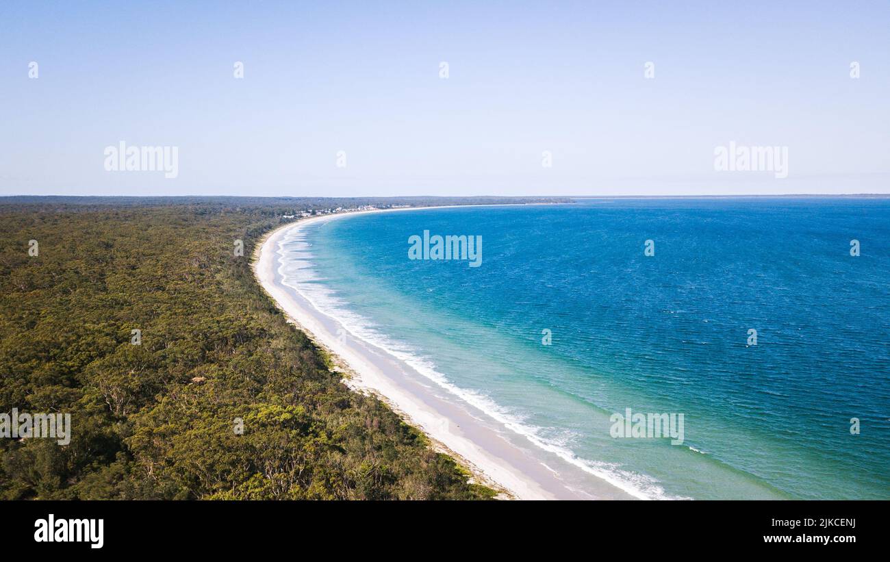 An aerial view of a beautiful sea with foamy waves crashing on a sandy ...