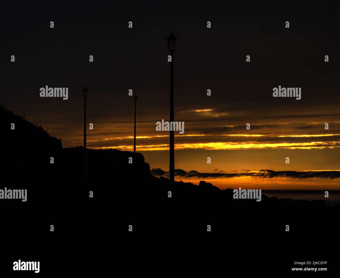 Sunset horizon at coast, with street lamp silhouettes and copyspace. Stock Photo