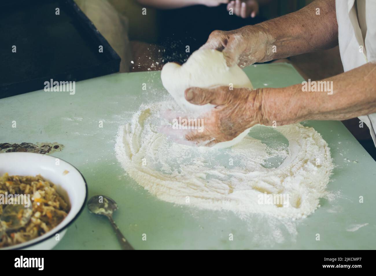 Old woman kneads dough for patties with flour Stock Photo