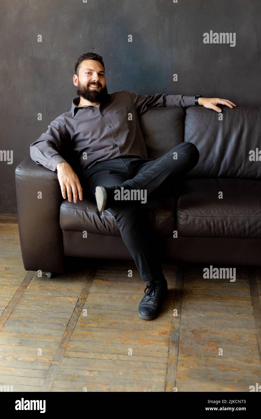 A man with a black beard is sitting on a leather sofa. businessman Stock Photo