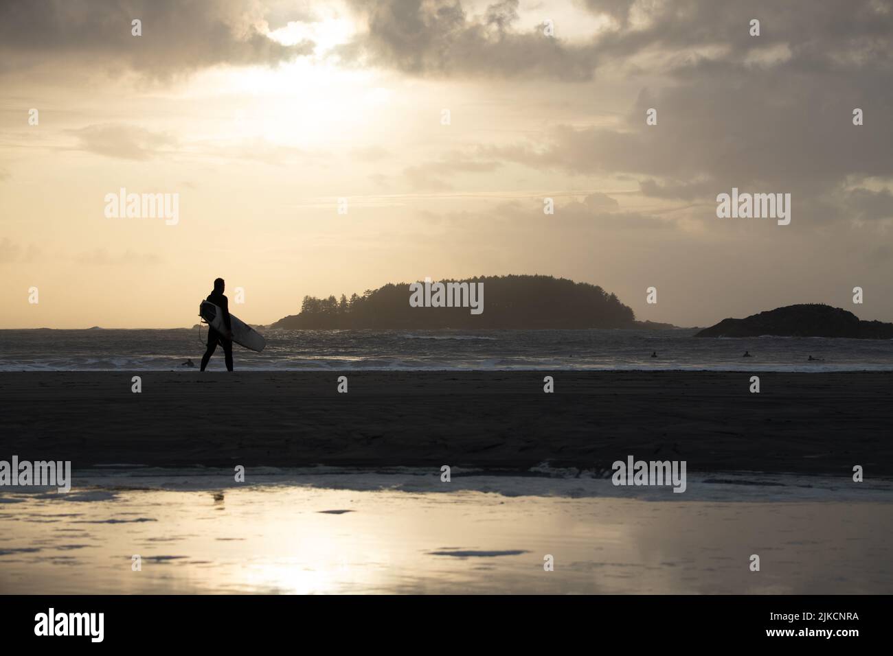 Surfer walking on the beach at sunset in Tofino, British Columbia Stock Photo