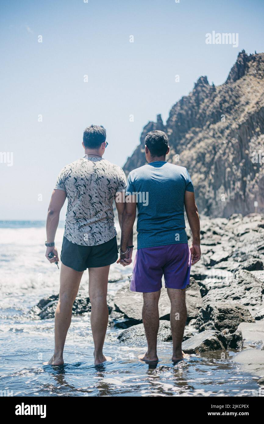 man with his boyfriend holding hands on beach on sunny day Stock Photo