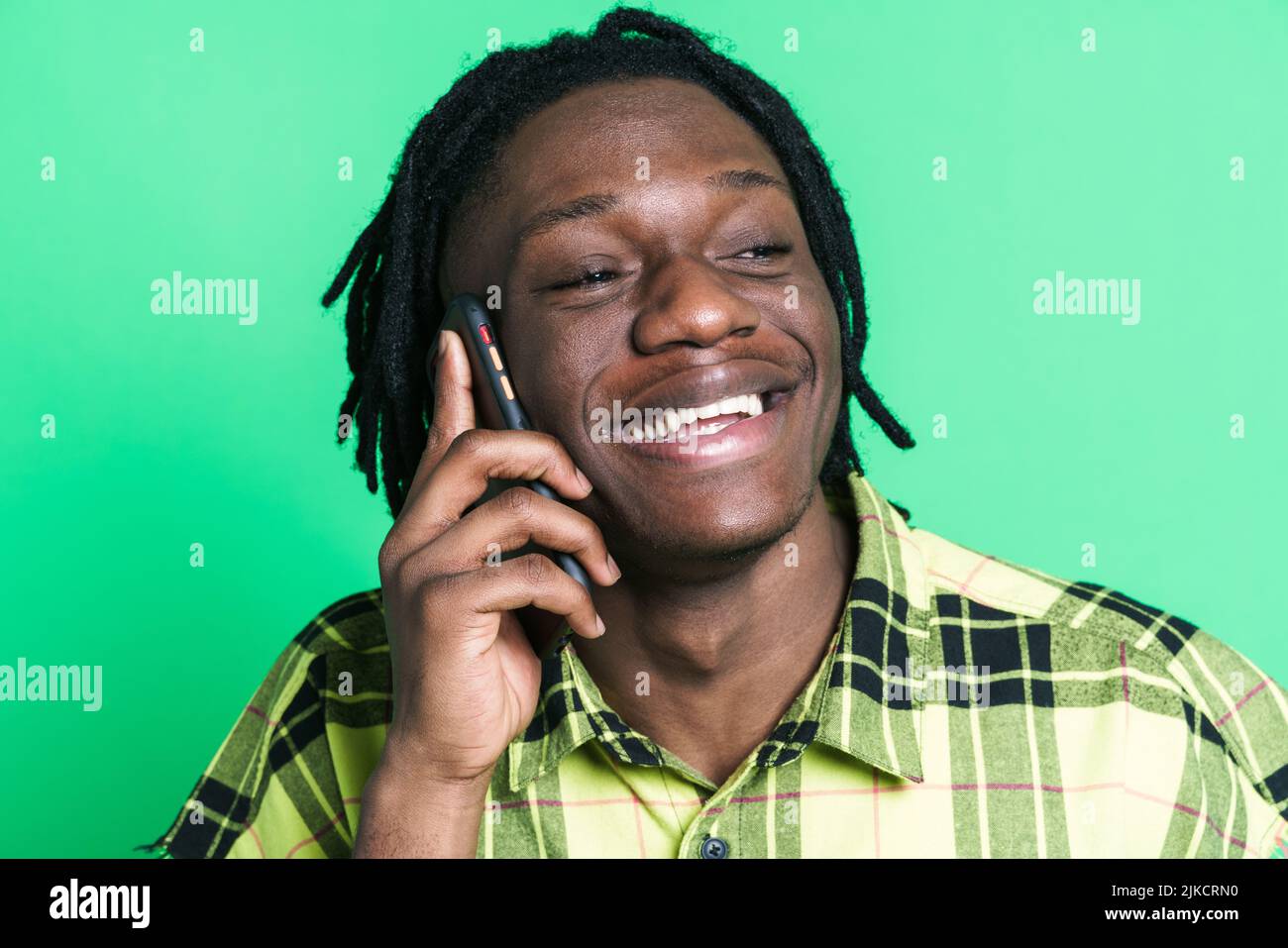 Young black man with dreadlocks talking on mobile phone isolated over green background Stock Photo