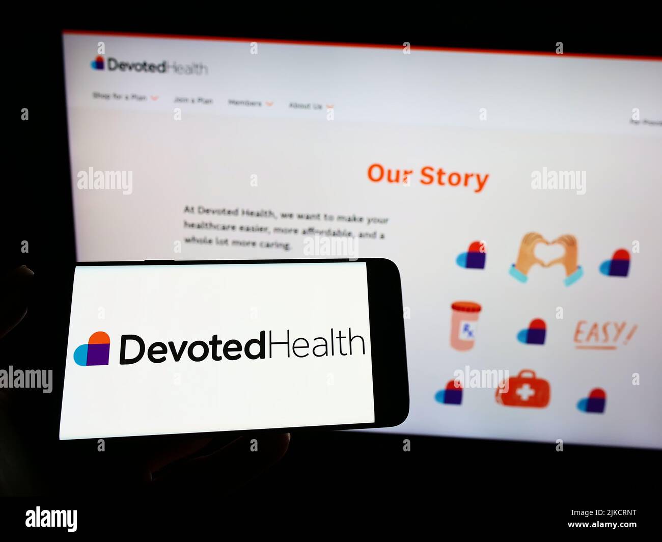 Person holding smartphone with logo of US healthcare company Devoted Health Inc. on screen in front of website. Focus on phone display. Stock Photo