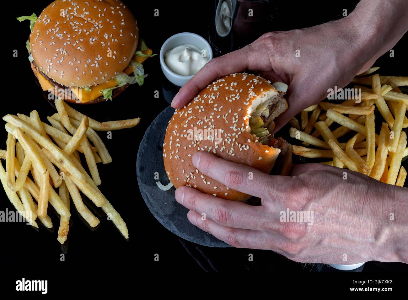 fresh tasty hamburger, french fries, cola on black glass with reflection, selective focus, top view. Fast food, junk food for quick snack. Stock Photo
