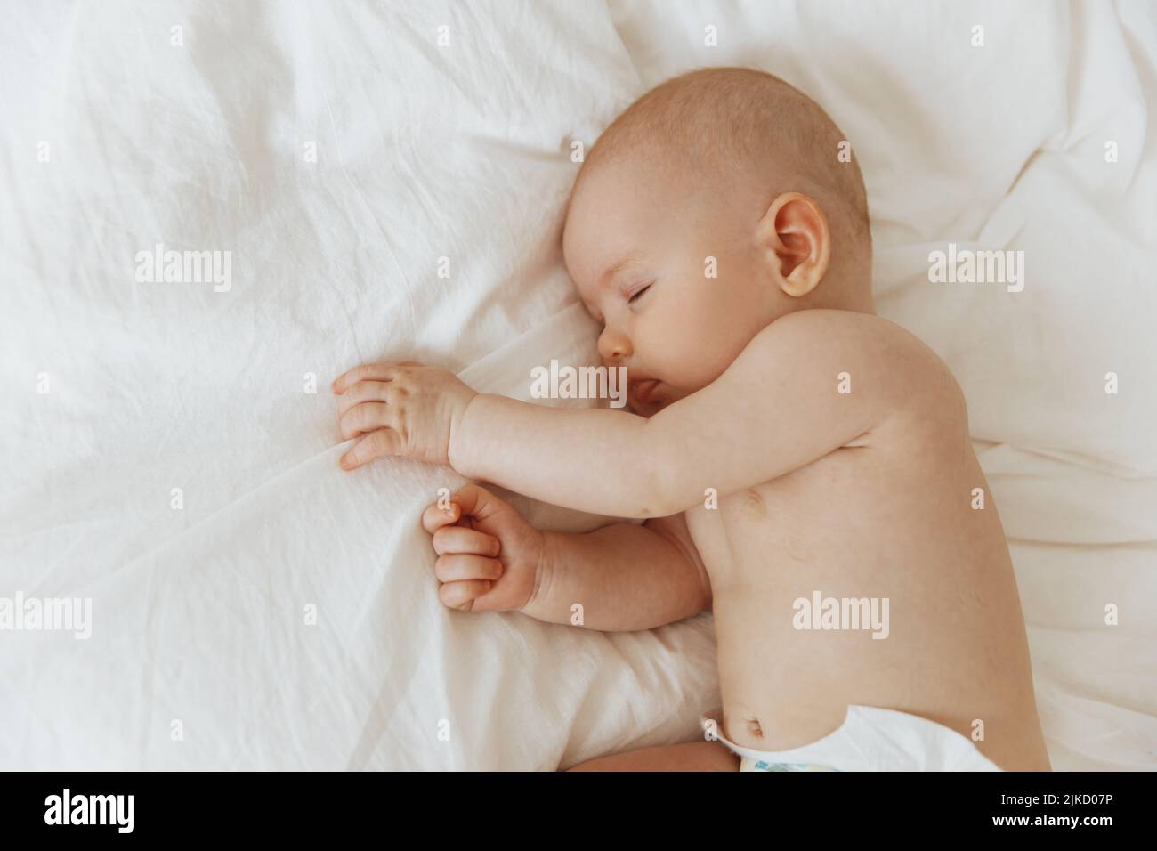 Beautiful little baby sleeps peacefully, lying on his side in bed indoors, relaxing during his daytime nap with his eyes closed. Toddler child napping Stock Photo
