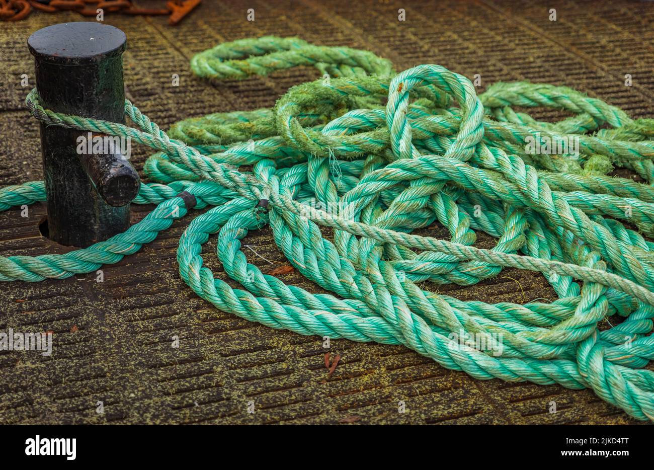 Mooring Bollard with rope on pier by the sea. Green Port rope. Mooring rope. Rope for fastening ships and cargo. Nobody Stock Photo