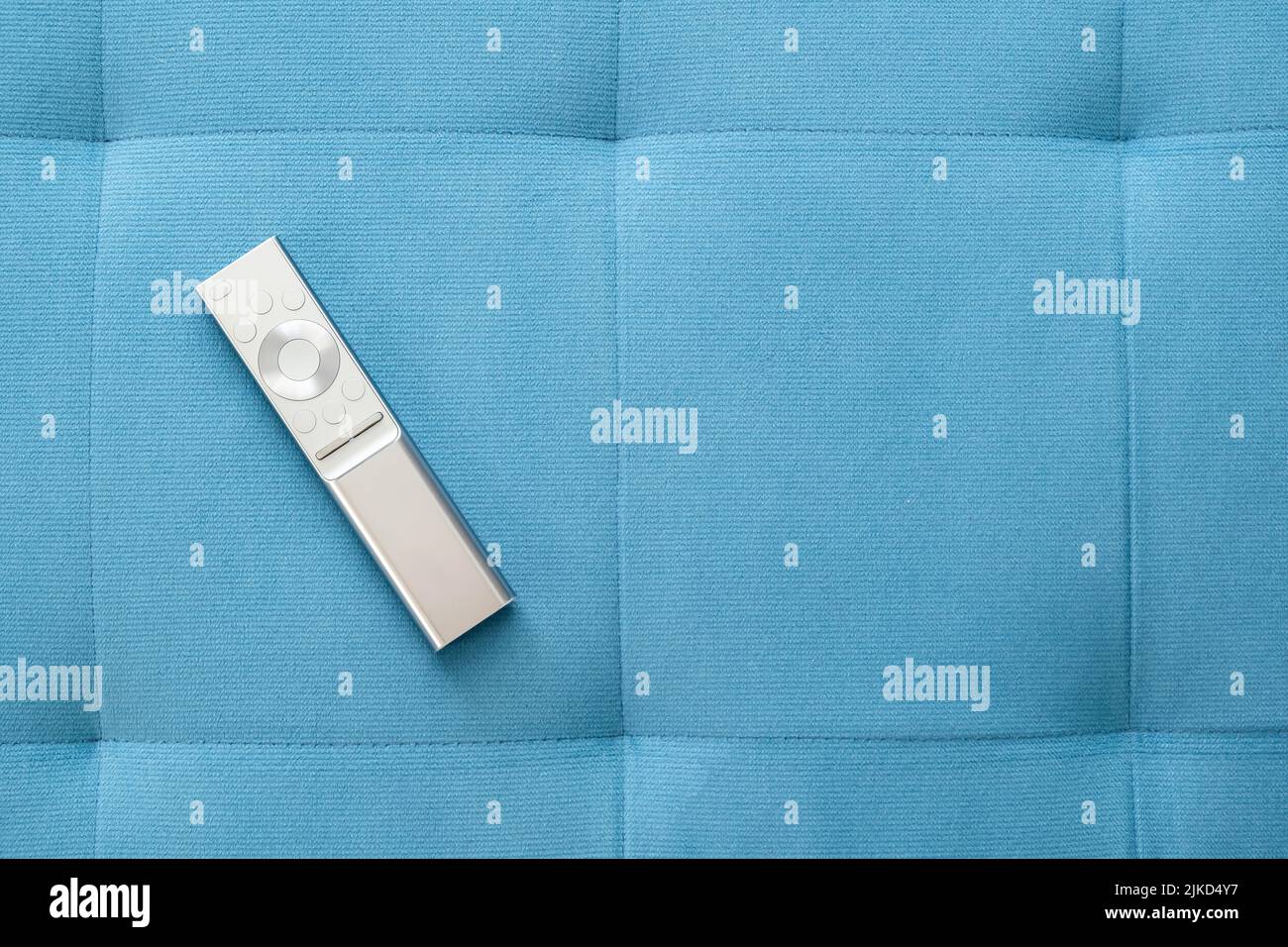 One single simple sliver smart TV remote control laying on a blue sofa pillow at home, object top view, closeup, nobody. Leisure, rest, watching TV sy Stock Photo