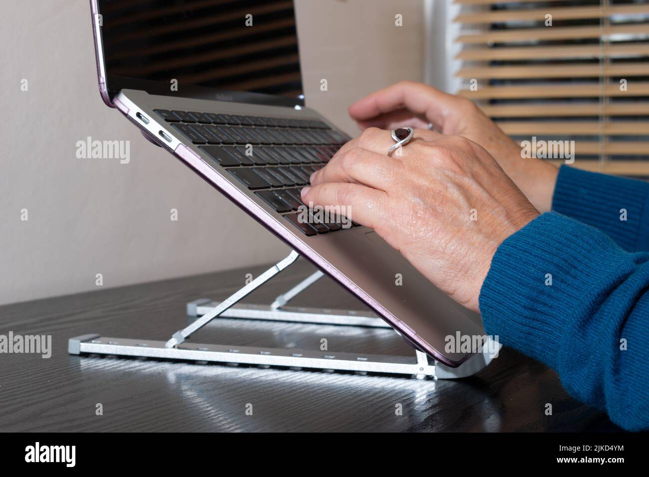 Laptop stand for wrist protection and neck posture. Foldable adjustable stand with hands typing on laptop screen raised to eye height in home office. Stock Photo