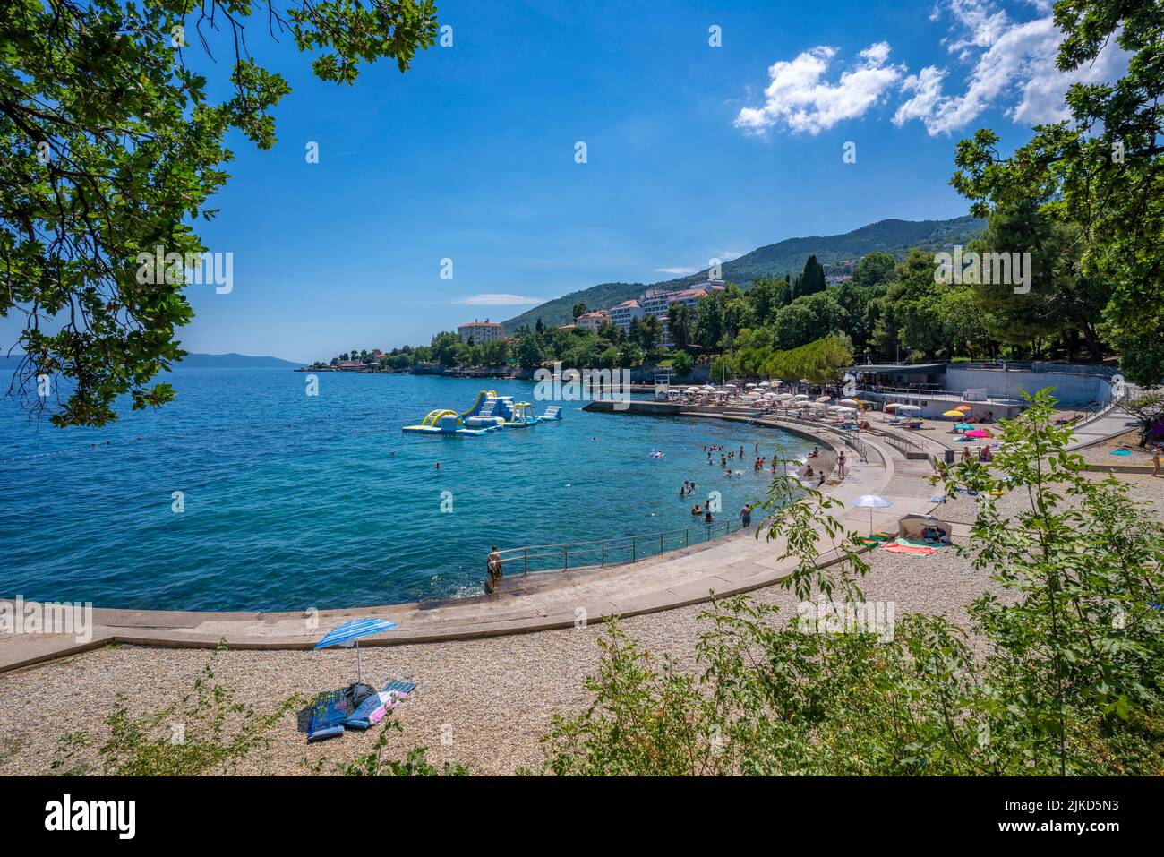 Holiday makers on tree lined pebble beach and Adriatic Sea at Lovran, Kvarner Bay, Eastern Istria, Croatia, Europe Stock Photo