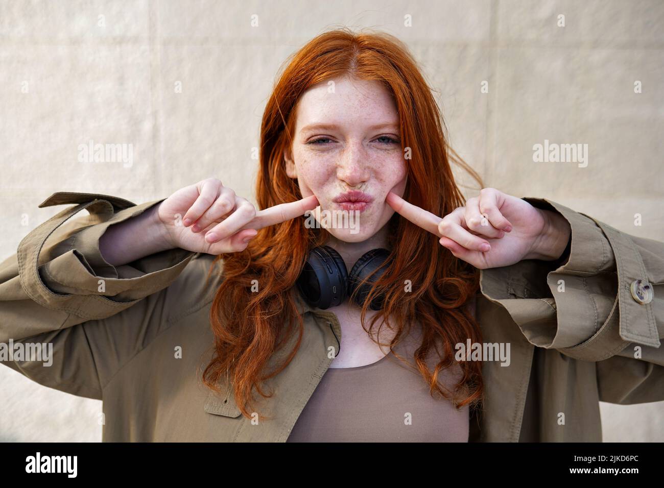 Happy funny teen redhead girl looking at camera on urban wall background. Stock Photo
