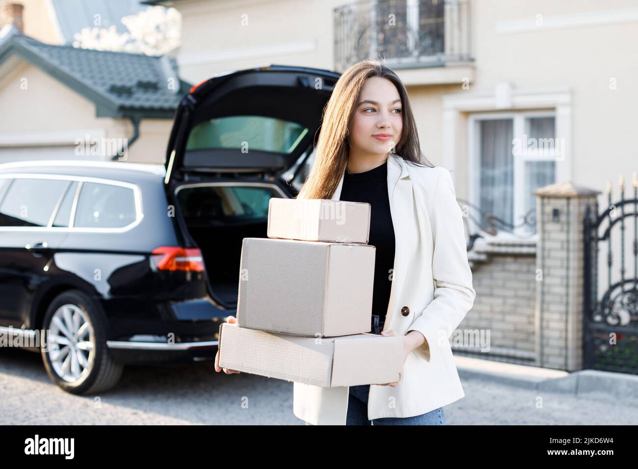 Young business woman picking up parcels from a car trunk, coming home by car. Stock Photo