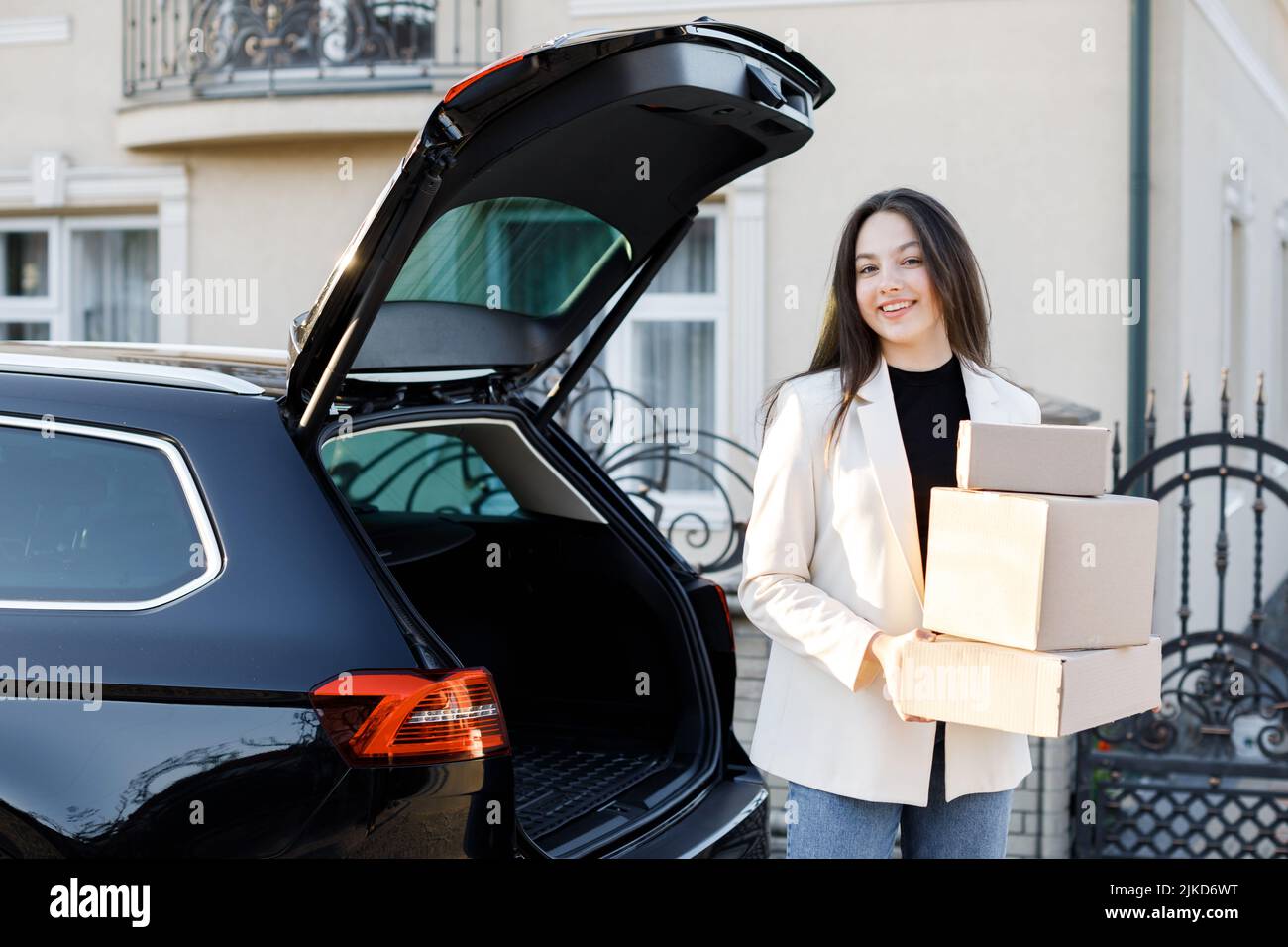 Young business woman picking up parcels from a car trunk, coming home by car Stock Photo