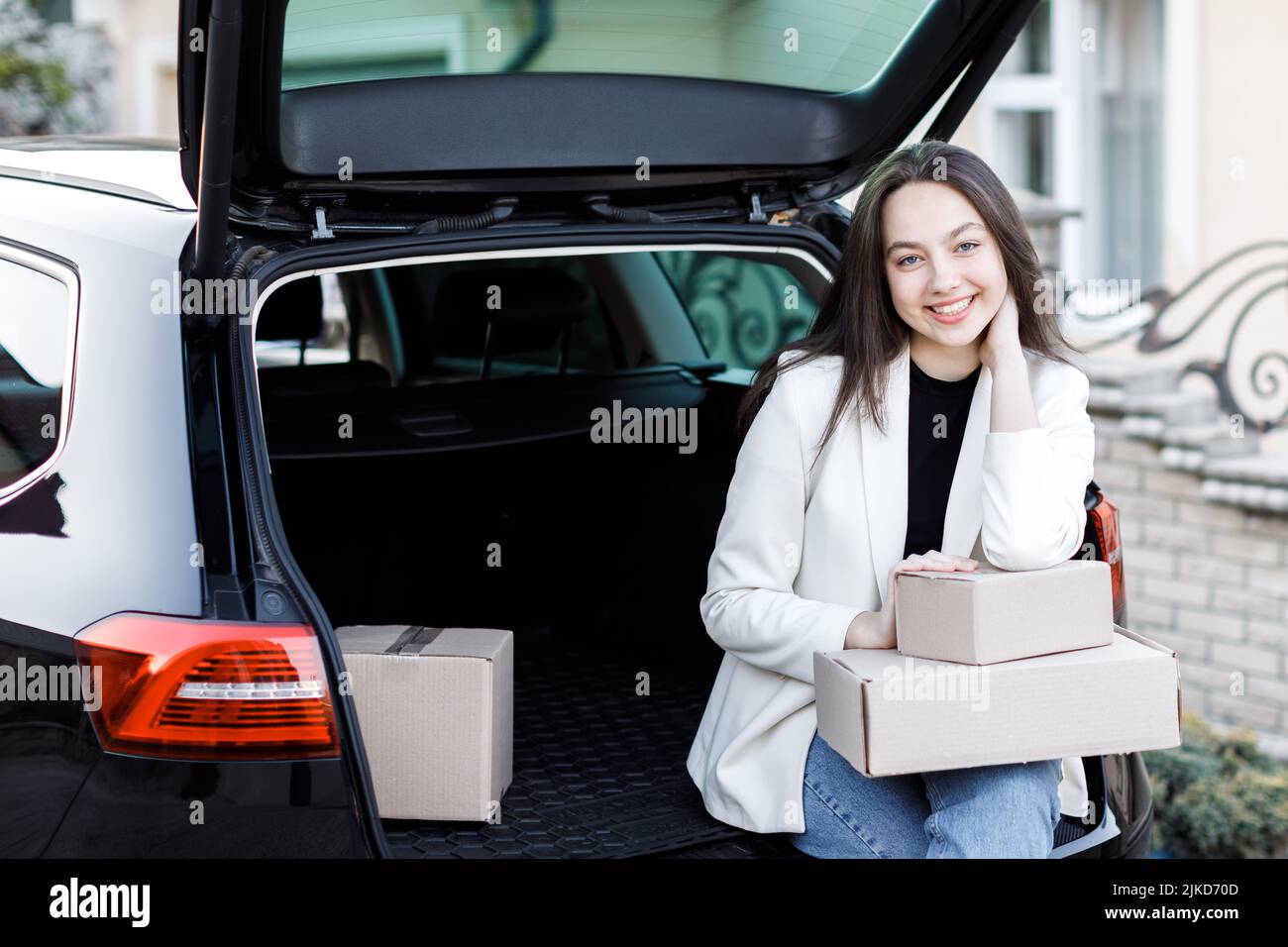 Girl sitting in the trunk of the car, holding boxes in his hands and smiling, looking at the camera Stock Photo