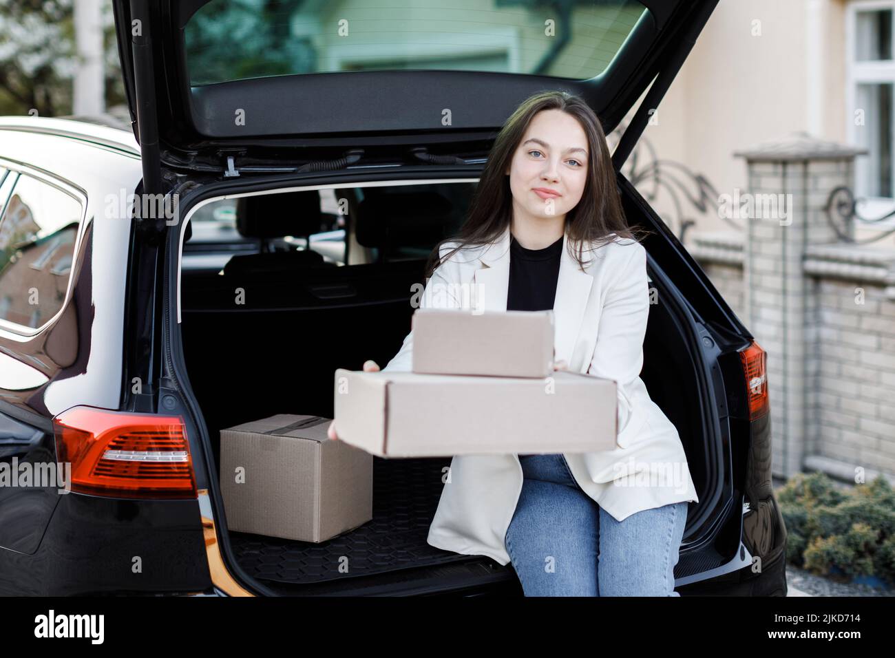 The girl sits in the trunk of the car and shows the boxes forward in front of the camera Stock Photo