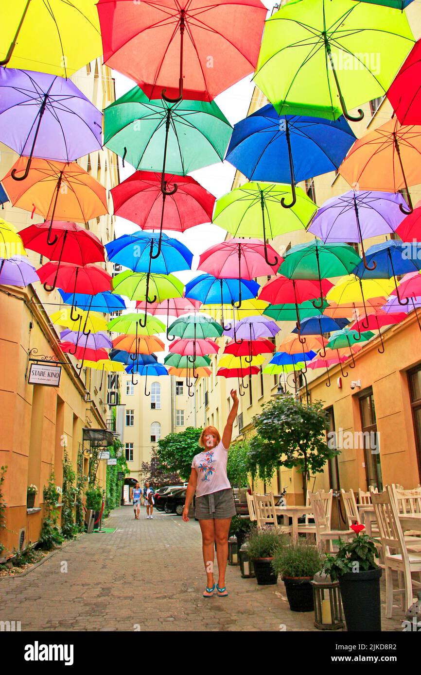 Street decoration. woman standing under colored umbrellas hanging at top. Set of different umbrellas. Local landmark. Cafe decoration in Lodz. Stock Photo