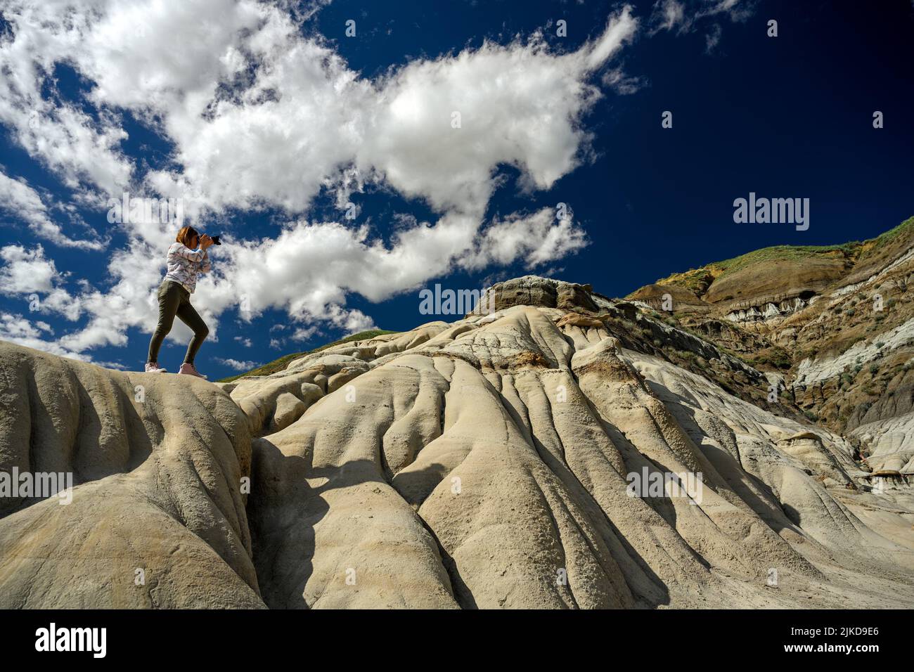 Tourist woman standing on a sandstone and photographing the Hoodoos and rock formations in the Canadian Badlands, Drumheller, Alberta, Canada. Stock Photo