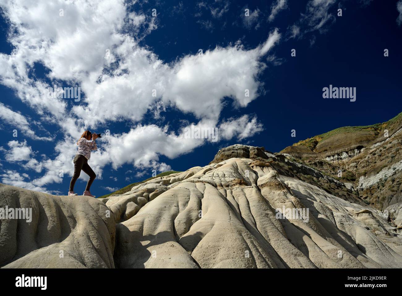 Tourist woman standing on a sandstone and photographing the Hoodoos and rock formations in the Canadian Badlands, Drumheller, Alberta, Canada. Stock Photo