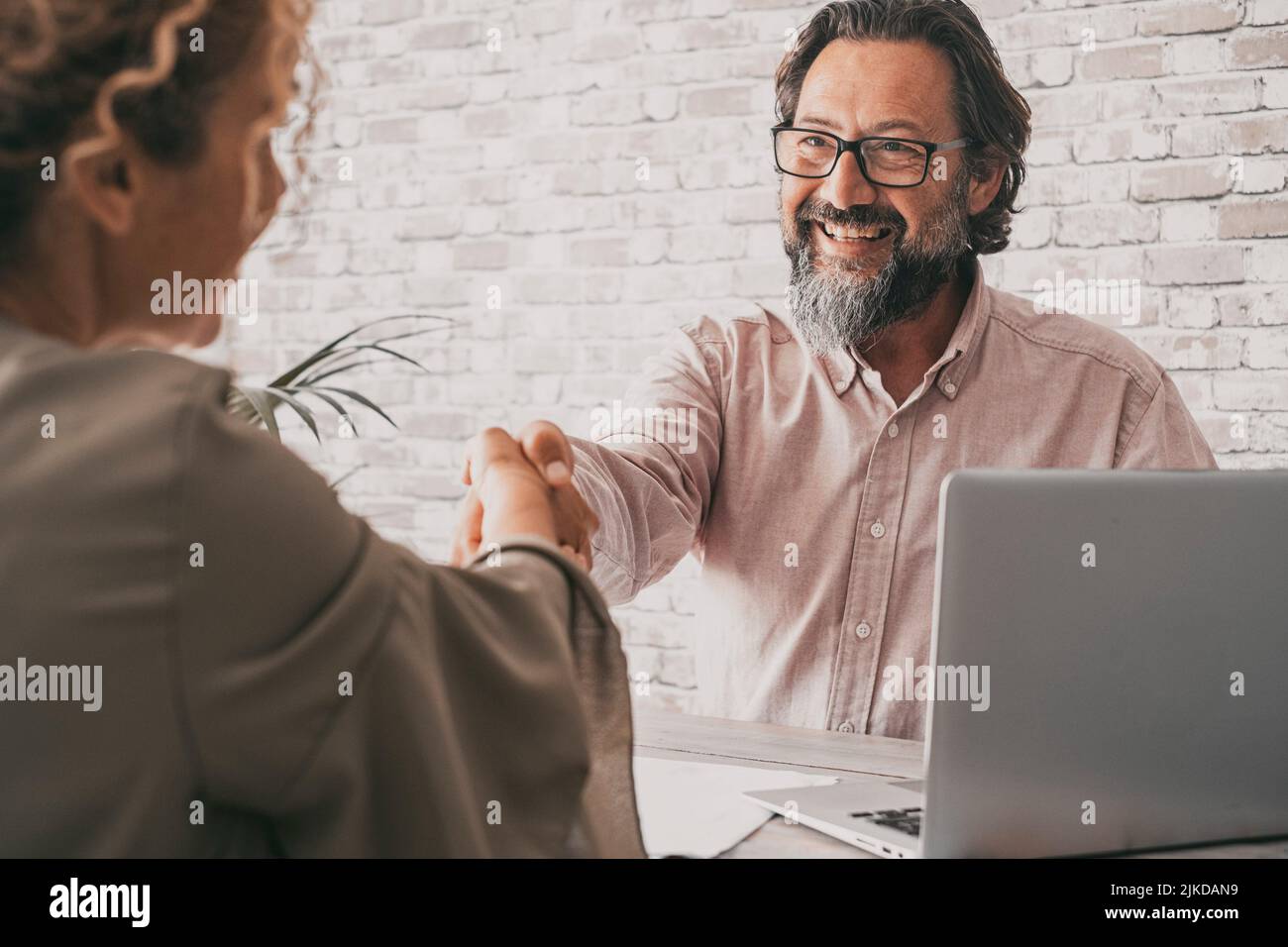 Couple of seller and buyer holding hands to sign an agreement. Confident professional business man give hand to woman client sitting at the desk in Stock Photo