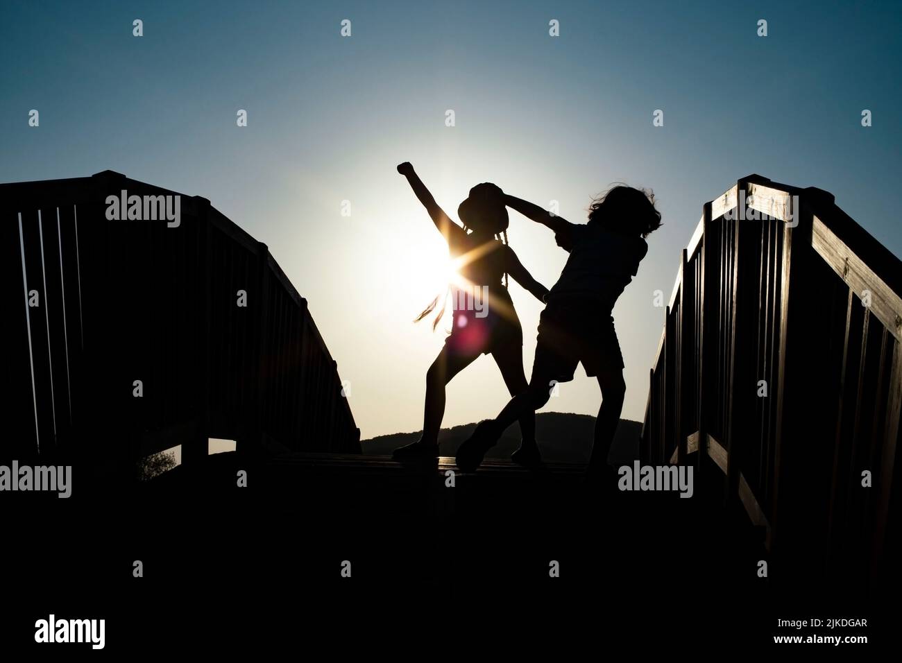Boy and girl silhouettes dancing on a bridge against the sunset sun ...