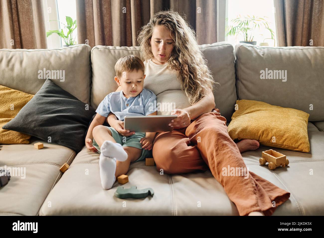 Young pregnant woman and little boy watching cartoons or movie for children or communicating in video chat while resting at home Stock Photo Alamy