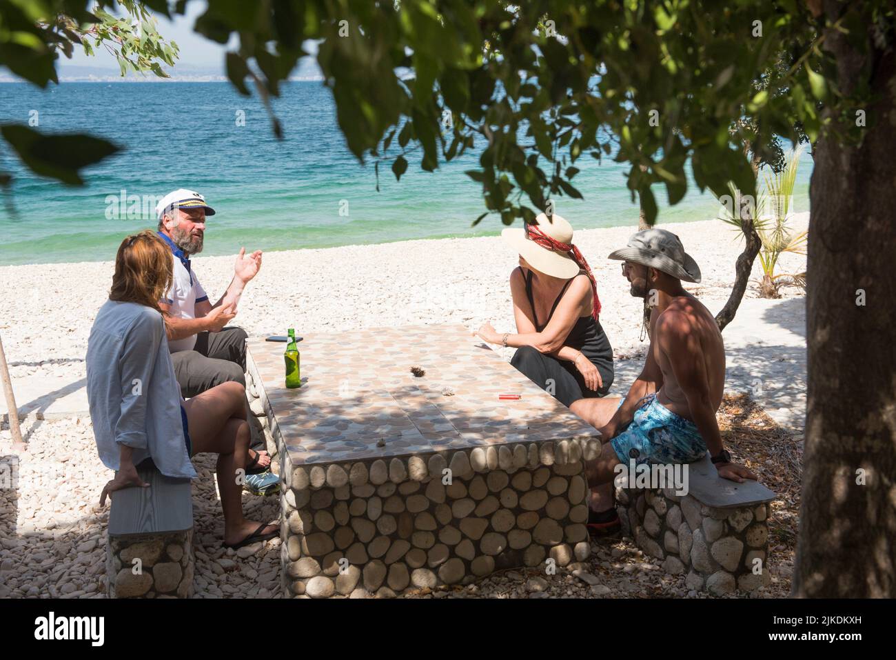 Four persons sitting at a table on the Beach in Zhanpovel Bay, Peninsula of Karaburun, within the Karaburun-Sazan Marine Parc, Vlore bay, Albania, Stock Photo