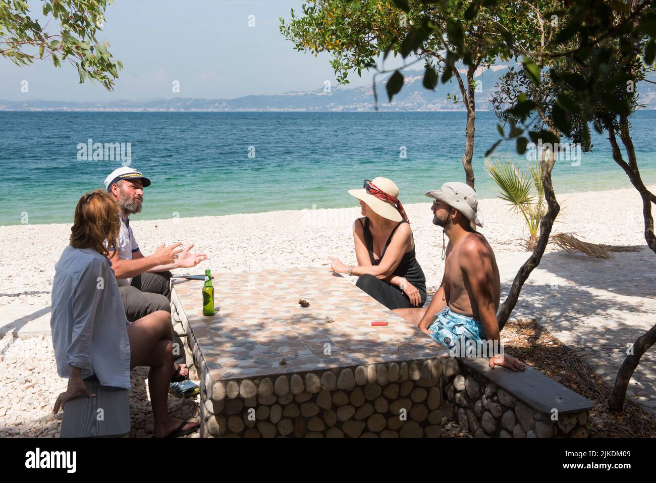 Four persons sitting at a table on the Beach in Zhanpovel Bay, Peninsula of Karaburun, within the Karaburun-Sazan Marine Parc, Vlore bay, Albania, Stock Photo