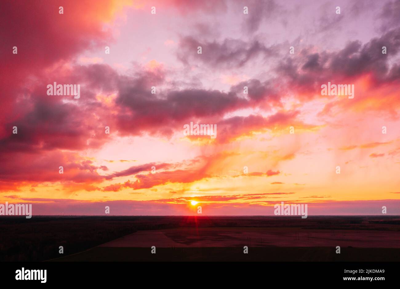Sunset sunrise colorful sky over field or meadow. Bright dramatic sky and dark ground. Countryside landscape under scenic amazing natural bright Stock Photo