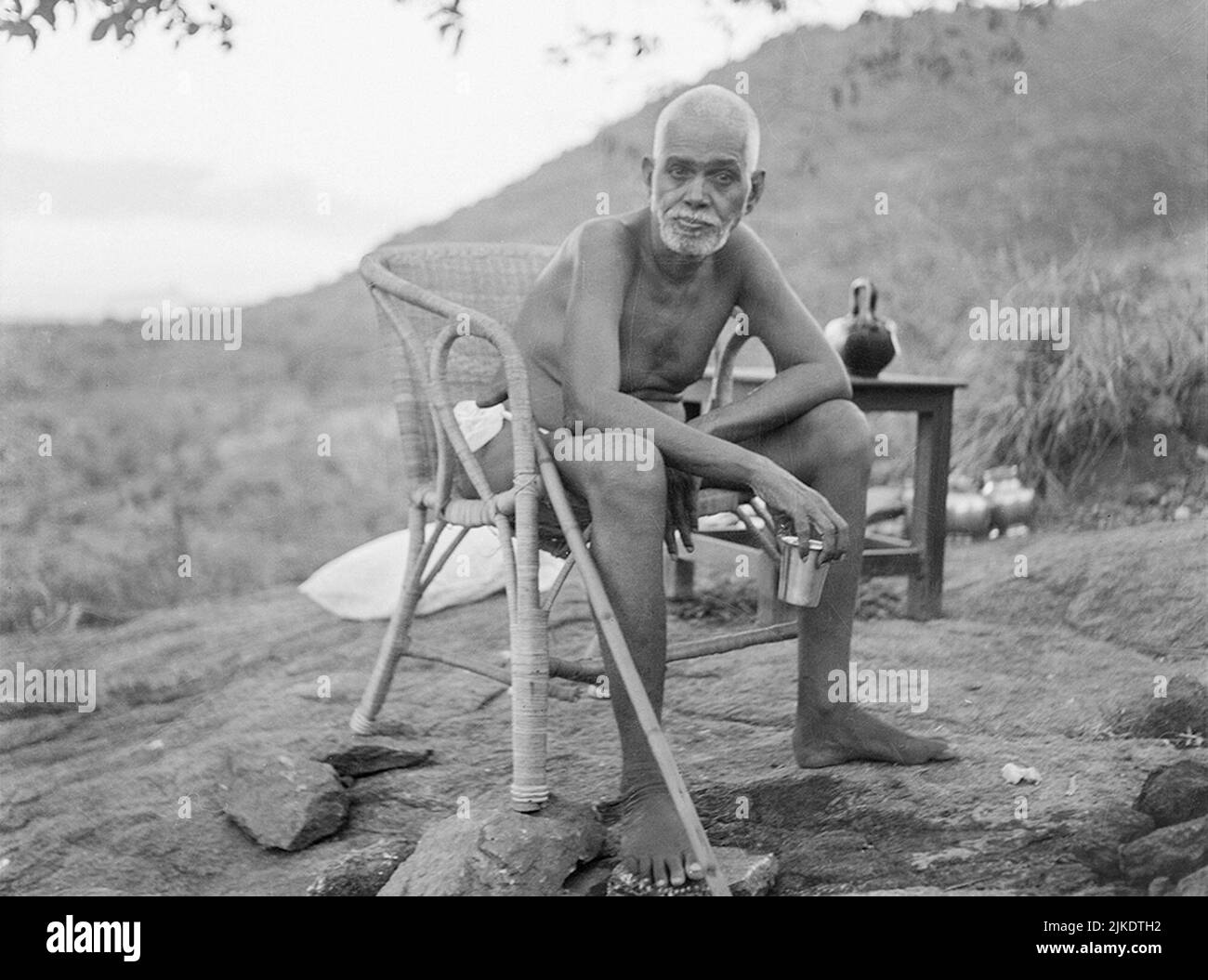 Indian sage Sri  Ramana Maharshi (1879-1950) sits in a chair bending over, with the holy hill Arunachala in the background, Tiruvannamalai, India Stock Photo
