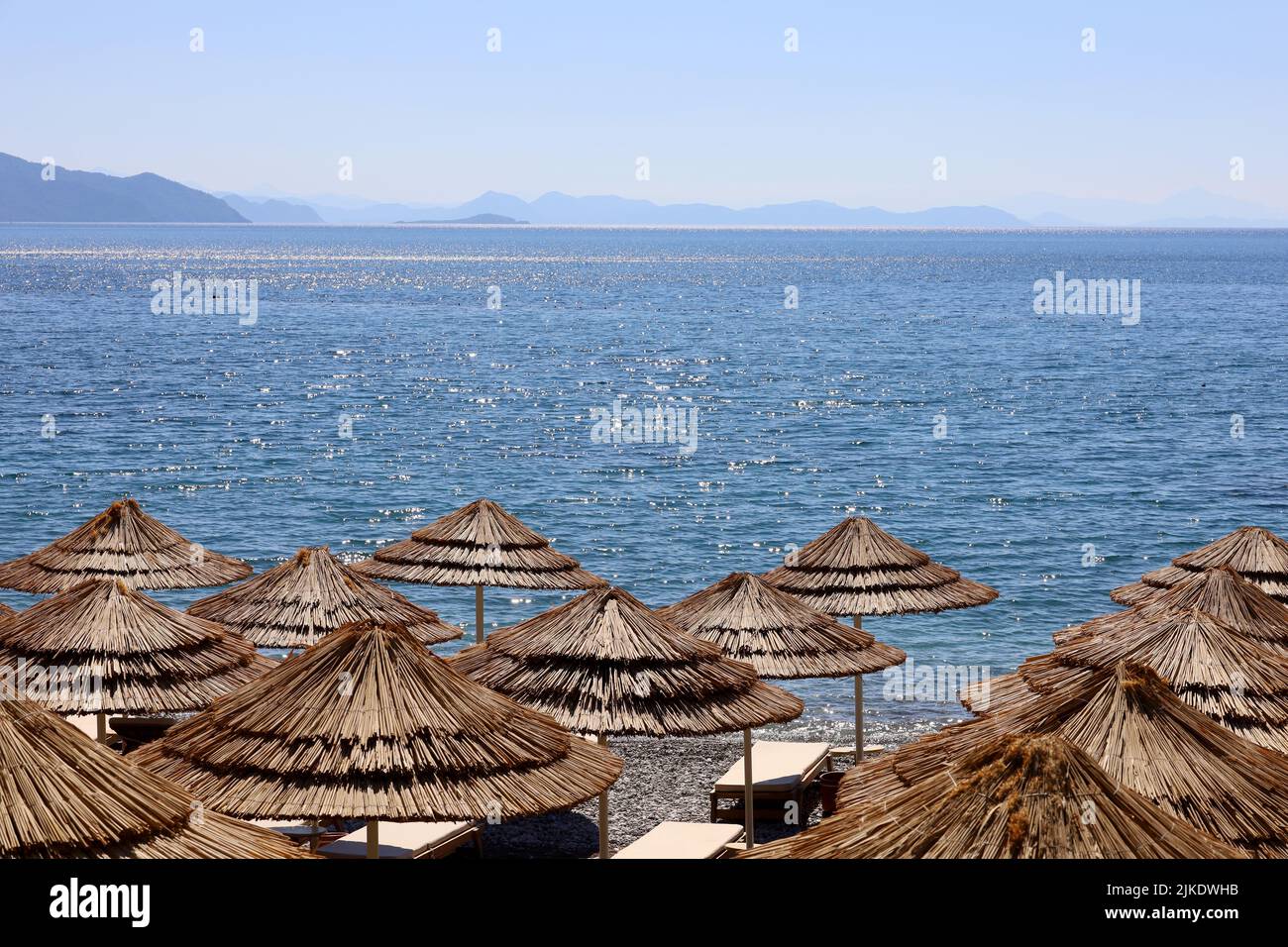 Empty pebble beach with wicker parasols and deck chairs. Picturesque view to blue sea and mountains in mist, luxury summer resort Stock Photo