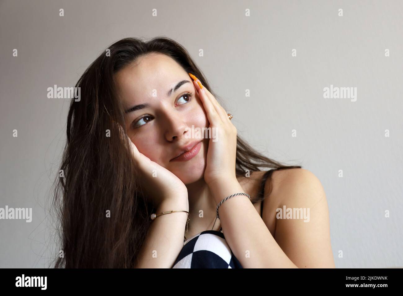 Portrait of attractive happy girl with long hair touching her face with her hands with orange acrylic nails. Concept of female beauty, dreamy mood Stock Photo