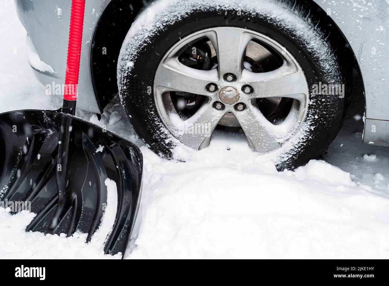 Snow shovel front of car wheel in white snowy day. Winter day routine