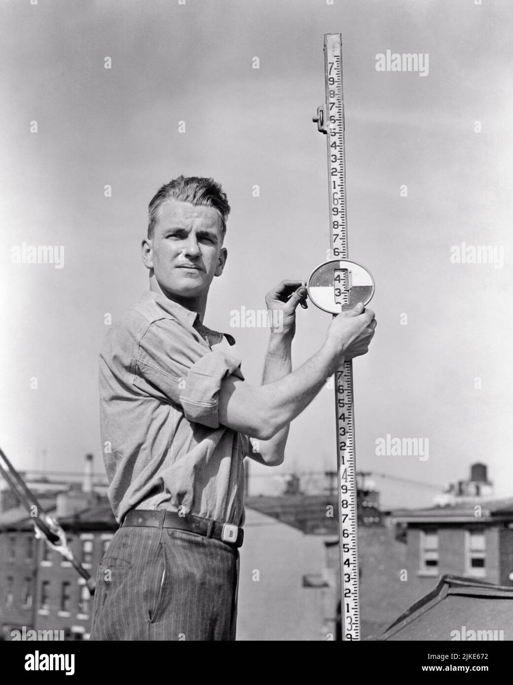 1940s MAN ASSISTING SURVEYORS ON CONSTRUCTION SITE BY HOLDING A LEVEL STAFF FOR MEASUREMENT - i41 HAR001 HARS HEAD AND SHOULDERS BUILD BASE CAREERS RECOVERY LABOR BETTER EMPLOYMENT OCCUPATIONS ERECT ERECTING INFRASTRUCTURE EMPLOYEE FACILITIES SURVEYORS ASSISTING COOPERATION CORE LEVEL MID-ADULT MID-ADULT MAN STAFF SYSTEMS BLACK AND WHITE CAUCASIAN ETHNICITY ECONOMY HAR001 LABORING OLD FASHIONED Stock Photo