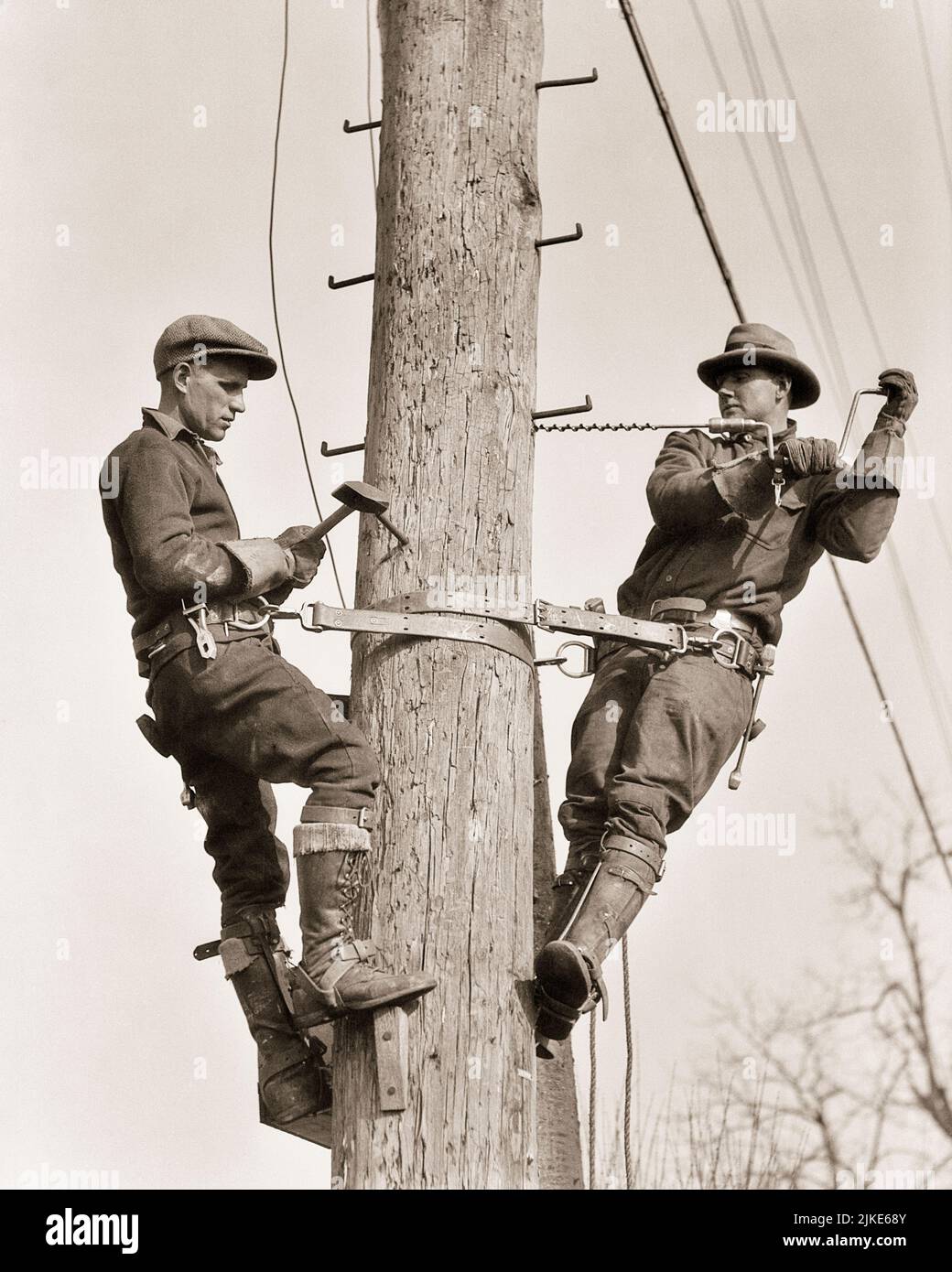1930s TWO MEN WORKING ON UTILITY POLE DRILLING HOLES FOR INSTALLATION OF METAL BRACKETS - i604 HAR001 HARS SKILLS BUILD DRILLING BASE CAREERS LOW ANGLE RECOVERY LABOR BETTER EMPLOYMENT OCCUPATIONS HOLES UTILITY INFRASTRUCTURE EMPLOYEE FACILITIES CORE MID-ADULT MID-ADULT MAN SYSTEMS BLACK AND WHITE CAUCASIAN ETHNICITY ECONOMY HAR001 INSTALLATION LABORING OLD FASHIONED Stock Photo