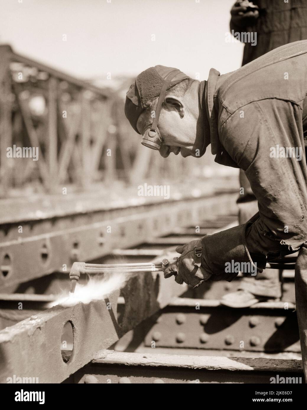 1930s MAN WEARING GOGGLES USING A BLOW TORCH CUTTING OLD GIRDERS ON A BRIDGE - i819 HAR001 HARS SKILL OCCUPATION STRUCTURE SKILLS HEAD AND SHOULDERS BUILD PROTECTION BASE CAREERS RECOVERY LABOR BETTER EMPLOYMENT OCCUPATIONS USING ERECT GIRDERS ERECTING INFRASTRUCTURE EMPLOYEE FACILITIES CORE MID-ADULT MID-ADULT MAN SYSTEMS BLACK AND WHITE CAUCASIAN ETHNICITY ECONOMY HAR001 LABORING OLD FASHIONED Stock Photo