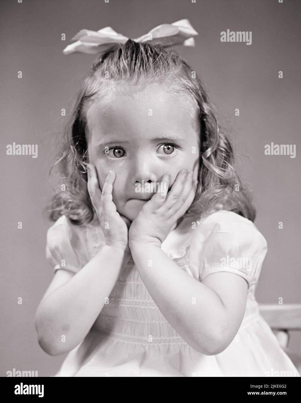 1940s LITTLE GIRL WITH BOW ON TOP OF HER HEAD HANDS TO HER CHEEKS IN SURPRISED AMAZED GESTURE OH MY MOMENT LOOKING OFF CAMERA - j10479 HAR001 HARS TROUBLED AMAZED B&W CONCERNED SADNESS WIDE CHEEKS FEELING GESTURES MOOD MOMENT GLUM WIDE-EYED EMOTION EMOTIONAL EMOTIONS JUVENILES MISERABLE STARTLED ALARMED BLACK AND WHITE CAUCASIAN ETHNICITY HAR001 OLD FASHIONED Stock Photo