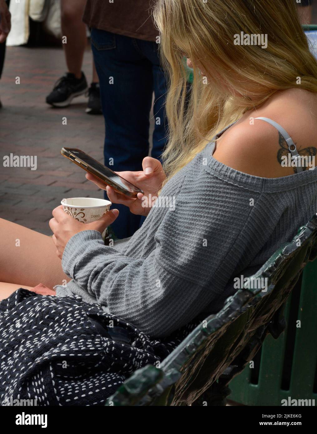 A young woman uses her smartphone while sitting on a bench in Santa Fe, New Mexico. Stock Photo
