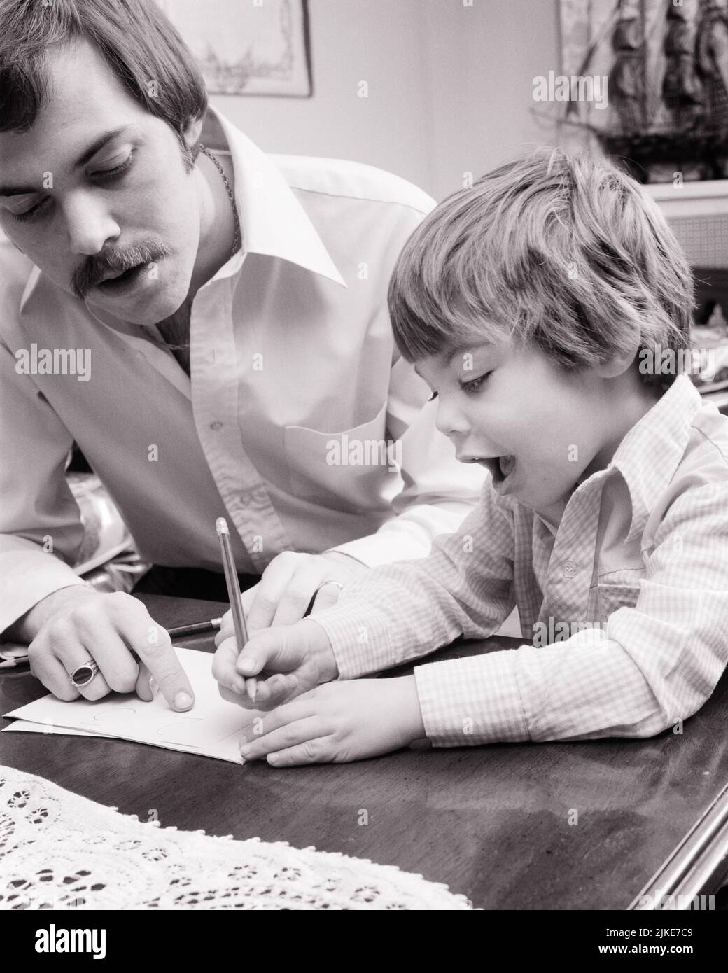 1970s MAN FATHER HELPING BOY HIS EXCITED EAGER YOUNG SON TO PRINT WRITE HIS NAME IN LETTERS WITH A PENCIL - j14024 HAR001 HARS JUVENILE FACIAL COMMUNICATION YOUNG ADULT TEAMWORK SONS JOY LIFESTYLE HOME LIFE COPY SPACE HALF-LENGTH PERSONS INSPIRATION CARING MALES WRITE EXPRESSIONS FATHERS B&W GOALS SUCCESS MUSTACHE HAPPINESS HEAD AND SHOULDERS HIGH ANGLE DISCOVERY HIS NAME STRENGTH MUSTACHES DADS EXCITEMENT PROGRESS PRIDE OPPORTUNITY FACIAL HAIR CONCEPTUAL SUPPORT GROWTH JUVENILES PRECISION TOGETHERNESS YOUNG ADULT MAN BLACK AND WHITE CAUCASIAN ETHNICITY HAR001 OLD FASHIONED Stock Photo