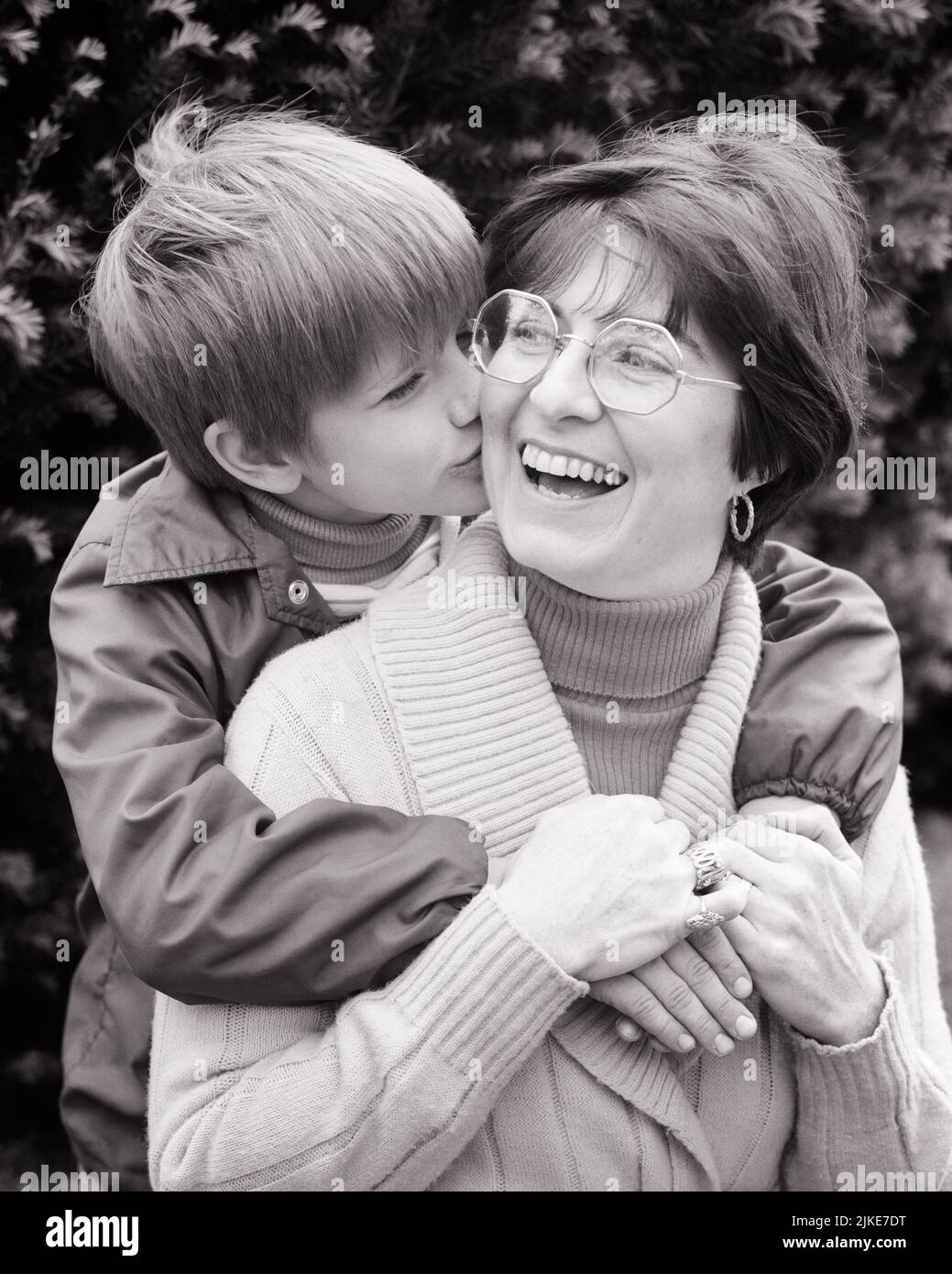 1970s LITTLE BOY HUGGING HIS MOTHER FROM BEHIND ARMS AROUND HER KISSING HER ON THE CHEEK MOM HOLDING HIS HAND LAUGHING - j14221 HAR001 HARS EXPRESSION OLD TIME SURPRISE NOSTALGIA HUGGING OLD FASHION 1 JUVENILE FACIAL LAUGH EMBRACE NECK STRONG SONS PLEASED FAMILIES JOY LIFESTYLE FEMALES HEALTHINESS HOME LIFE COPY SPACE FRIENDSHIP HALF-LENGTH HUG LADIES PERSONS CARING MALES EMBRACING EXPRESSIONS B&W HAPPINESS CHEERFUL HIS JOYFUL PERSONAL ATTACHMENT AFFECTION EMOTION JUVENILES MID-ADULT MID-ADULT WOMAN MOMS PECK SMOOCH BLACK AND WHITE CAUCASIAN ETHNICITY HAR001 OLD FASHIONED Stock Photo