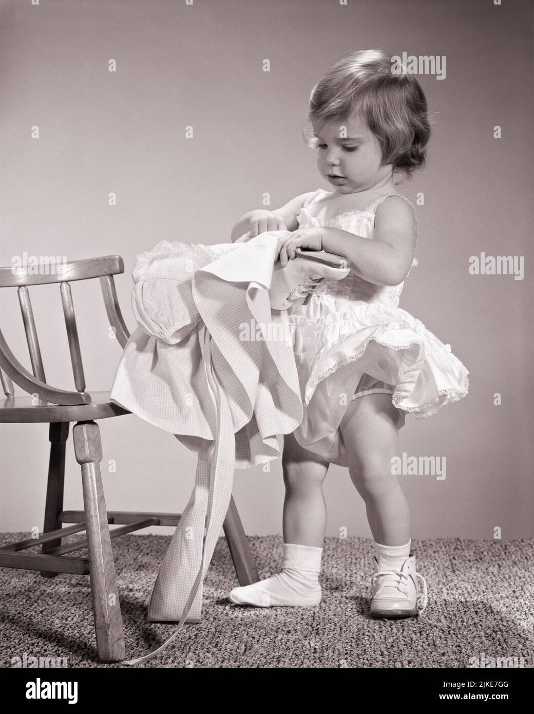 1960s TODDLER GIRL GETTING DRESSED AND PUTTING ON A DRESS AND SHOES ALL BY HERSELF - j1584 HAR001 HARS DISCOVERY AND EXCITEMENT TRYING PRIDE CONCEPTUAL STYLISH ATTEMPTING DETERMINED FOCUSED GROWTH HERSELF JUVENILES BABY GIRL BLACK AND WHITE CAUCASIAN ETHNICITY HAR001 OLD FASHIONED Stock Photo