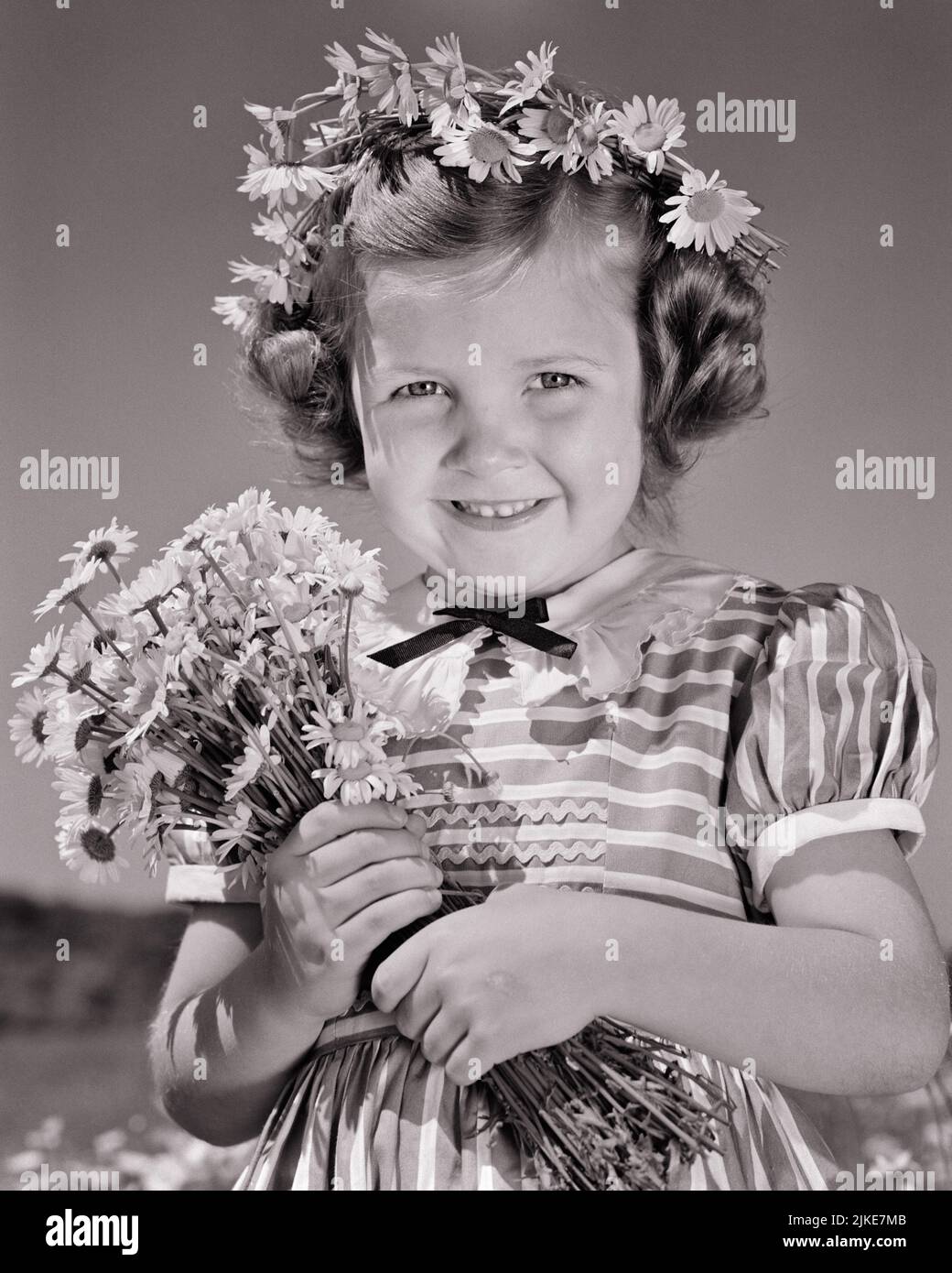 1940s LITTLE GIRL HOLDING A BOUQUET OF DAISIES AND CROWN OF DAISY IN HER HAIR SMILING WEARING A STRIPED DRESS LOOKING AT CAMERA - j1905 HAR001 HARS WINNING FLORAL RURAL HEALTHINESS NATURE COPY SPACE GARLAND HALF-LENGTH INSPIRATION CONFIDENCE B&W DAISY SUMMERTIME EYE CONTACT DAISIES DREAMS HAPPINESS CHEERFUL AND PRIDE SMILES JOYFUL STYLISH PLEASANT AGREEABLE CHARMING GROWTH JUVENILES LOVABLE PLEASING SEASON ADORABLE APPEALING BLACK AND WHITE CAUCASIAN ETHNICITY HAR001 OLD FASHIONED Stock Photo